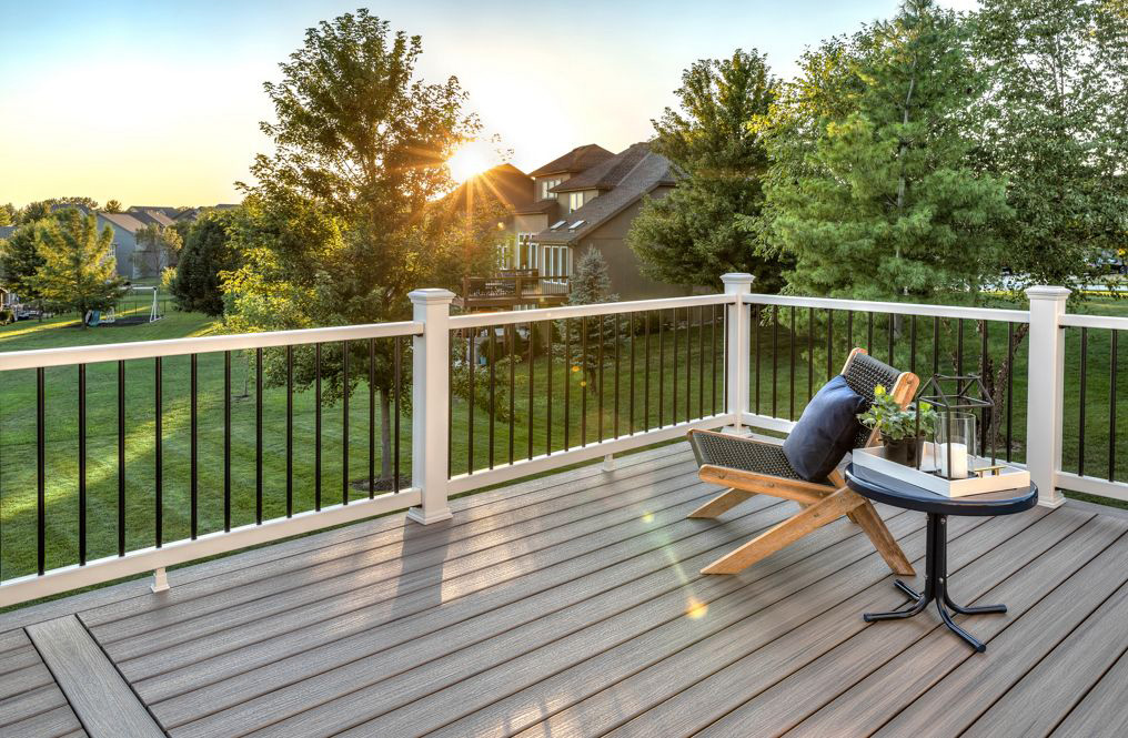 This image depicts a stunning deck with a Trex railing system. A chair and table are set on the deck while the sun sets in the background.