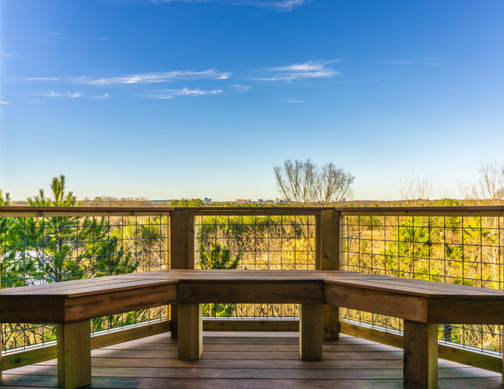 A deck has a built-in bench and railing system that allows people to see the gorgeous views of a field. 