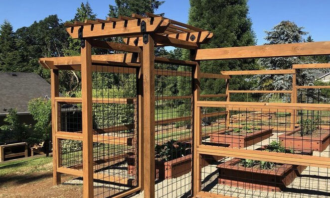 A garden is enclosed with a Hog Wire railing system and wood boards.